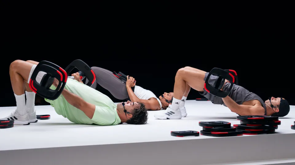 Fitness-Instruktorin Kylie Gates gibt Bodypump-Anfängertipps, während eine Teilnehmerin mit korrekter Technik Langhantelübungen ausführt, um die progressive Gewichtssteigerung zu demonstrieren.