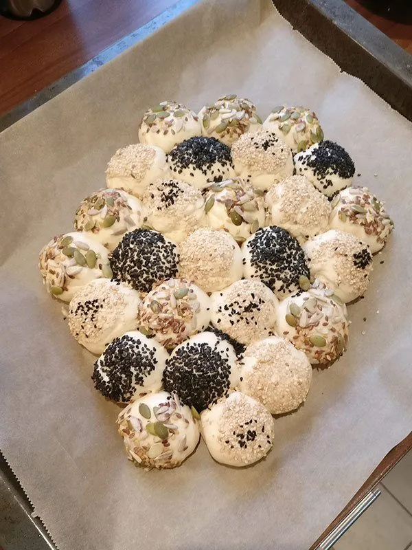 Fortgeschrittene Anordnung der Mini-Hefeteigbrötchen zu einer fast fertigen Brötchensonne auf dem Backpapier.
