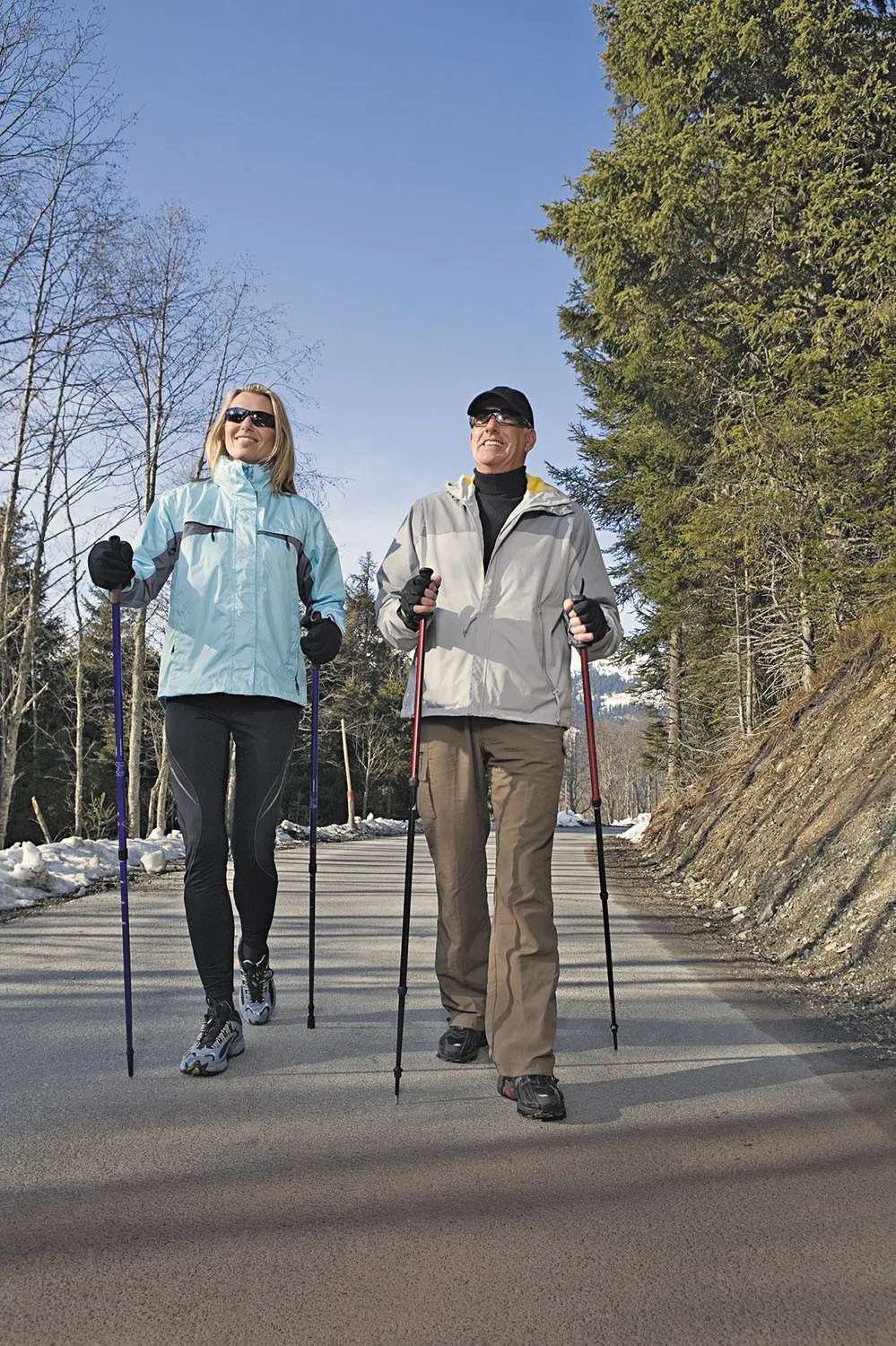 Frau beim Nordic Walking Sport in verschneiter Landschaft mit Stöcken und Sonnenschein
