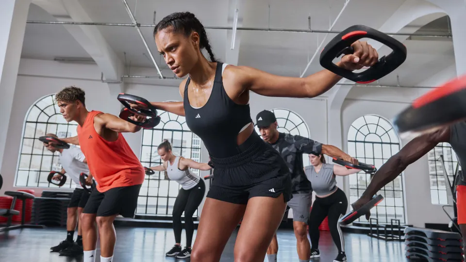 Frau führt Kniebeugen mit einer Langhantel bei einem Bodypump-Workout aus, um Muskeln aufzubauen und den Stoffwechsel für langfristigen Kalorienverbrauch anzukurbeln.