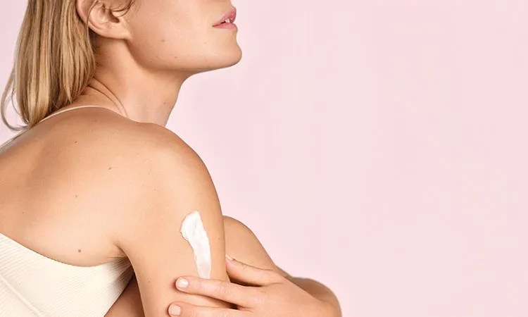 Frau trägt Feuchtigkeitscreme auf ihren juckenden Arm auf, ein effektives Hausmittel gegen Juckreiz