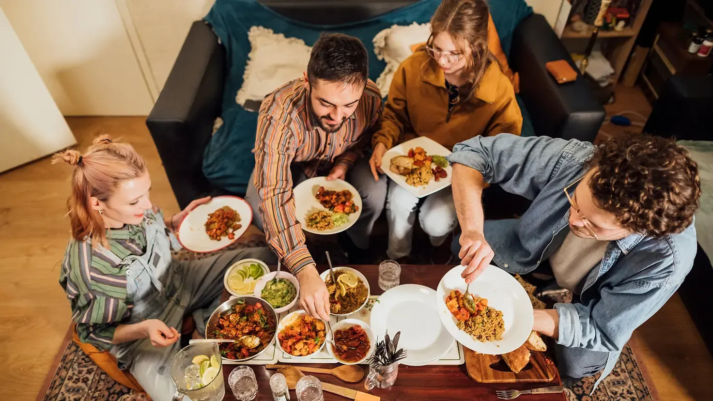 Freunde sitzen um einen Tisch und essen ein selbst gekochtes veganes Essen.