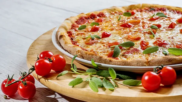 Frisch gebackene Pizza Margherita mit geschmolzenem Mozzarella und frischem Basilikum auf einem Holzbrett, im Hintergrund ein Holzofen.