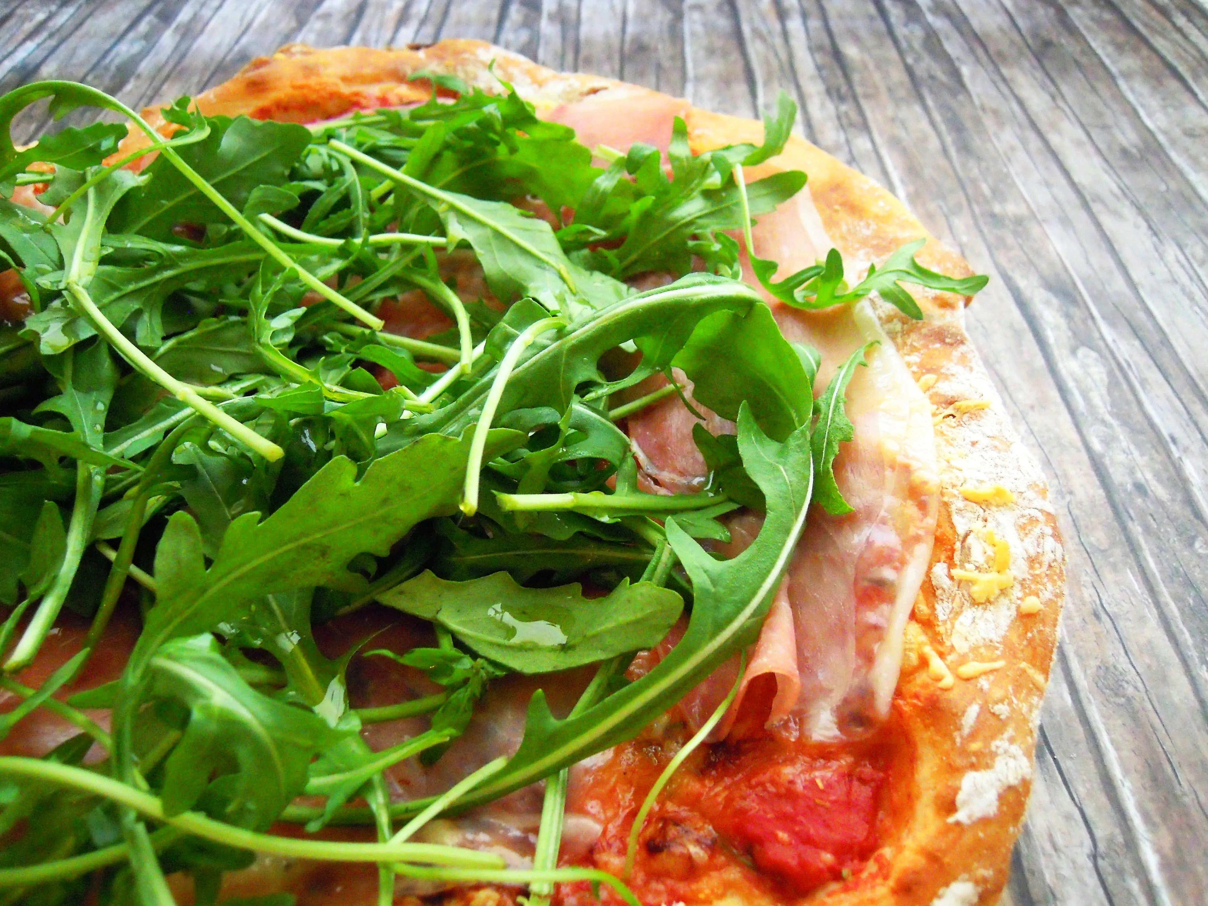 Frisch gebackene Rucola Pizza mit Prosciutto und Mozzarella auf einem Holzbrett, bereit zum Servieren.