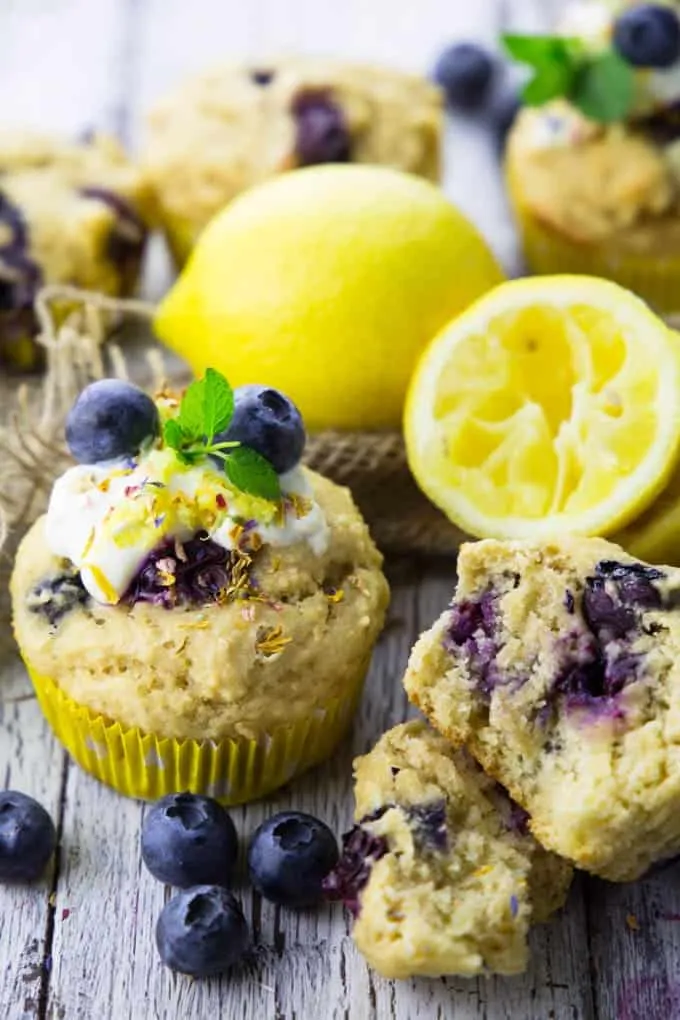 Frisch gebackene vegane Blaubeer-Zitronen-Muffins auf einem Holzbrett, umgeben von Zitronen und Blaubeeren.