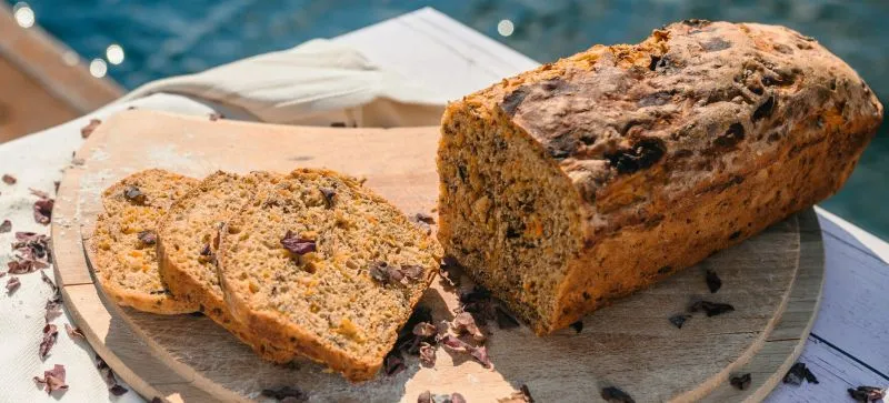 Frisch gebackenes Karottenbrot auf einem Holztisch, umgeben von frischen Karotten und Dulse Algenflocken. Der Fokus liegt auf der saftigen Krume und der appetitlichen Kruste.