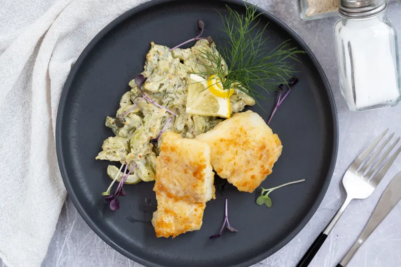 Frisch gebratener Kabeljau auf dem Teller, verfeinert mit einem Spritzer Zitronensaft für das perfekte Aroma.