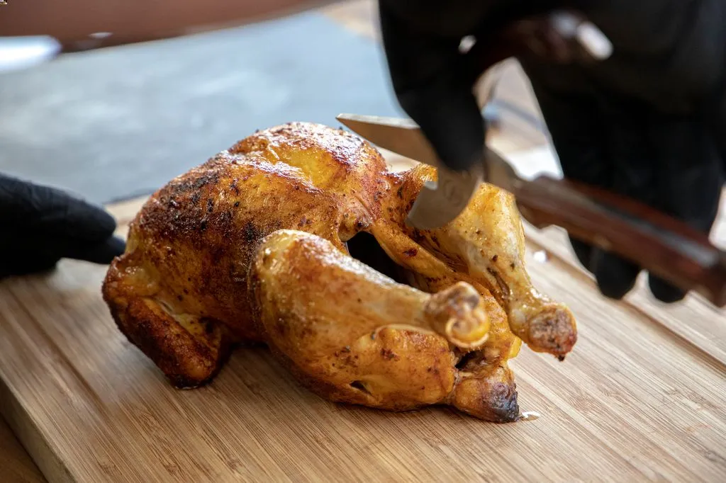 Frisch gegrilltes, knuspriges Hähnchen wird auf einem Holzbrett tranchiert