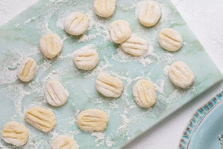 Frisch gekochte Gnocchi werden mit einer Schaumkelle aus dem Wasser gehoben, um auf einem Teller abzukühlen.