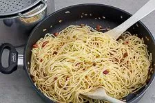 Frisch gekochte Spaghetti werden in der großen Pfanne mit dem duftenden Speck und seinem Fett vermengt, ein wichtiger Schritt für die Carbonara.