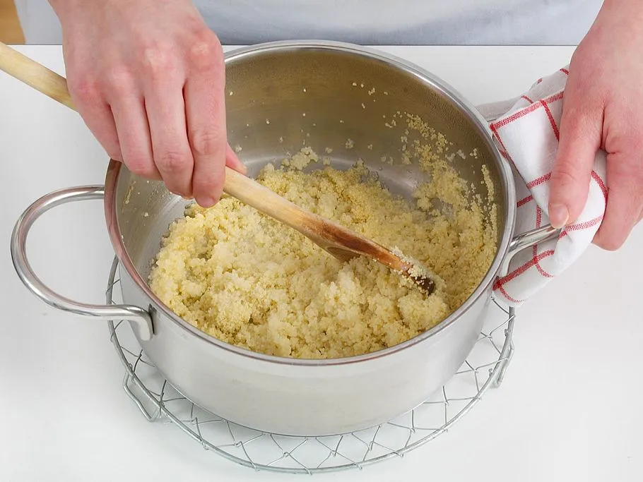 Frisch gekochter Couscous wird mit einer Gabel aufgelockert, um ein Verkleben der Körnchen zu verhindern.