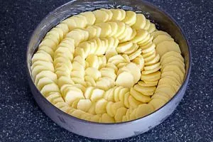 Frisch geschnittene Kartoffelscheiben und ihre gleichmäßige Anordnung in der runden Auflaufform
