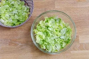 Frisch geschnittener Eisbergsalat, gewaschen und getrocknet, als erste Schicht für den Taco Salat in einer Glasschüssel.