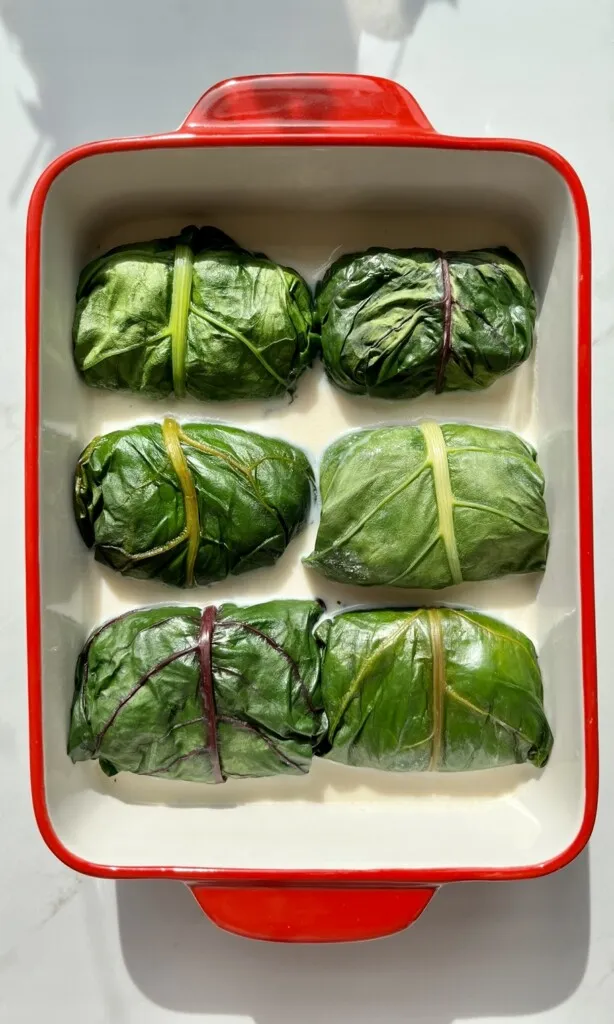 Frisch zubereitete Capuns mit geschmolzenem Schweizer Käse und Salsiz, servierfertig in einer Auflaufform.