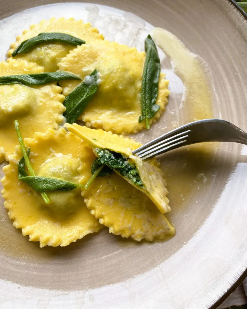 Frisch zubereitete Spinat-Ricotta-Ravioli in Salbeibutter geschwenkt, bereit zum Genießen. Die perfekte hausgemachte Pasta für jeden Anlass.