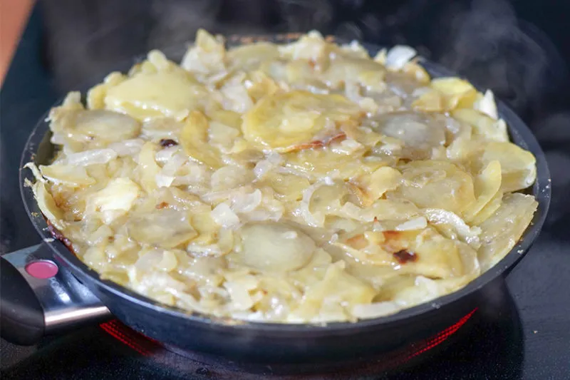 Frisch zubereitete Tortilla Española in einer Antihaftpfanne, bereit zum Wenden.