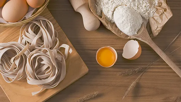 Frisch zubereiteter, handgemachter Nudelteig mit Eiern und Mehl auf einer bemehlten Arbeitsfläche, bereit zum Ausrollen.