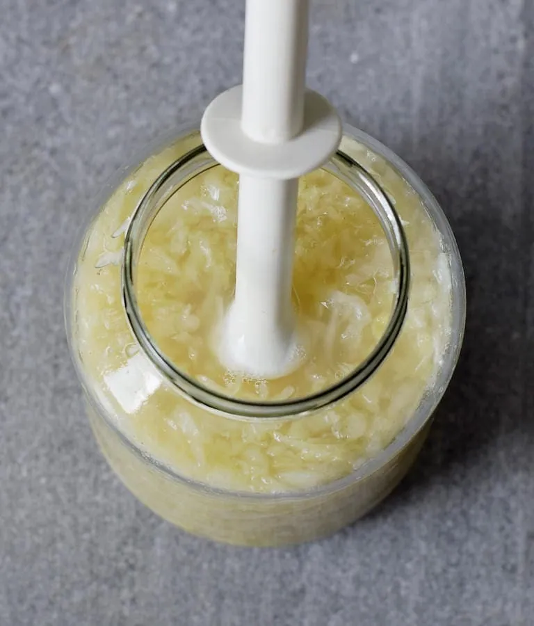 Frisch zubereitetes Sauerkraut wird mit einem Holzstößel fest in ein Glas gedrückt