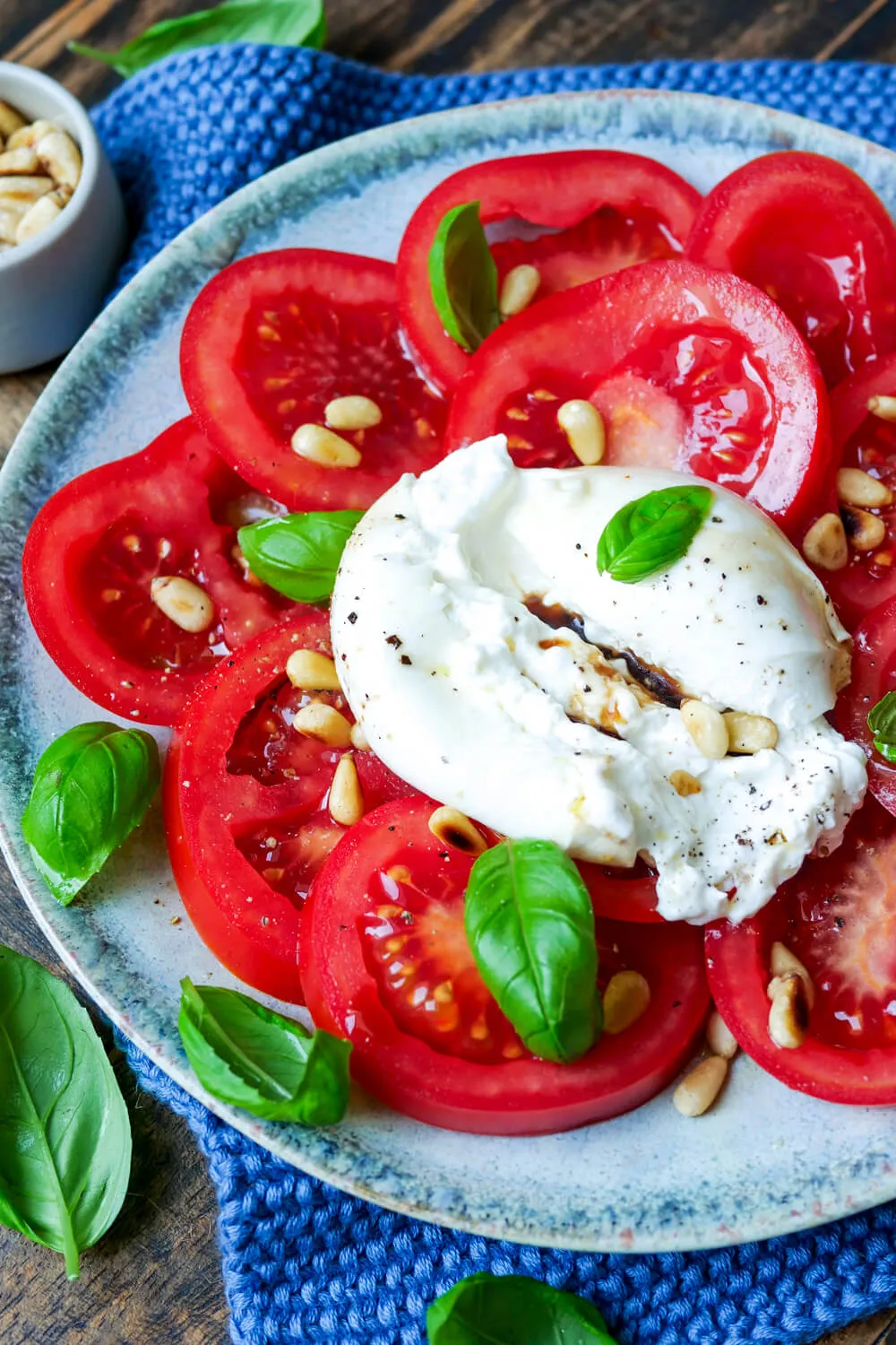 Frische Burrata mit reifen Tomatenscheiben, grünem Basilikum und gerösteten Pinienkernen als sommerliche Vorspeise.