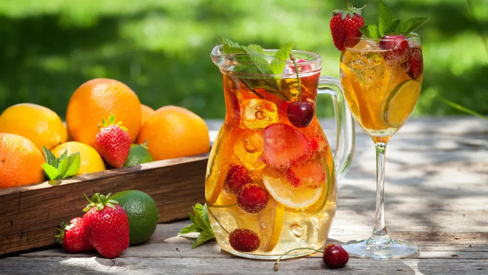 Frische Fruchtbowle mit bunten Früchten in einer Glaskaraffe, bereit zum Servieren auf einem Holztisch.