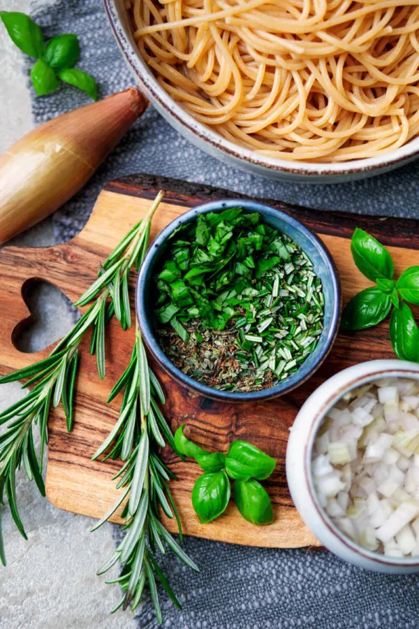 Frische gehackte Kräuter wie Basilikum, Rosmarin und Thymian auf einem Holzschneidebrett für die Tomatensoße