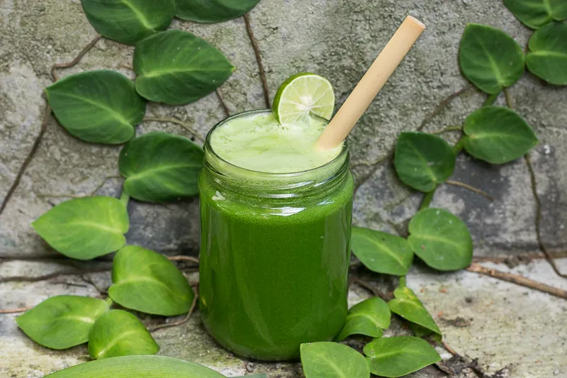 Frische grüne Säfte in Gläsern, bereit zum Genuss, mit Zutaten wie Spinat und Sellerie daneben.