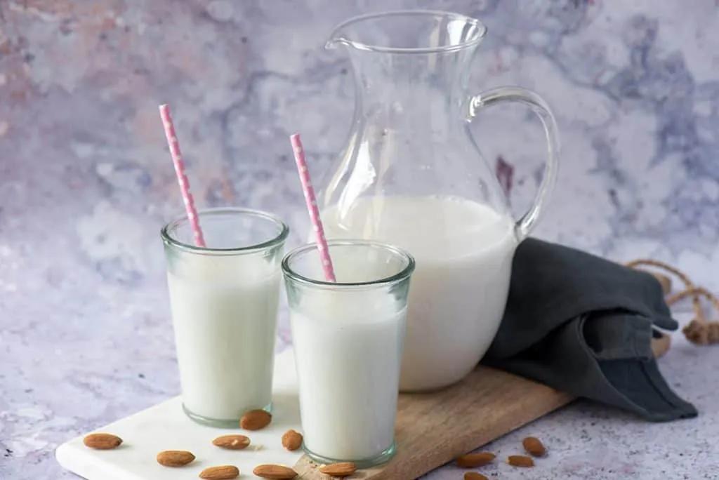 Frische hausgemachte Mandelmilch in einer Flasche mit Mandeln und Mandelmus im Hintergrund, perfekt als gesunde Milchalternative.