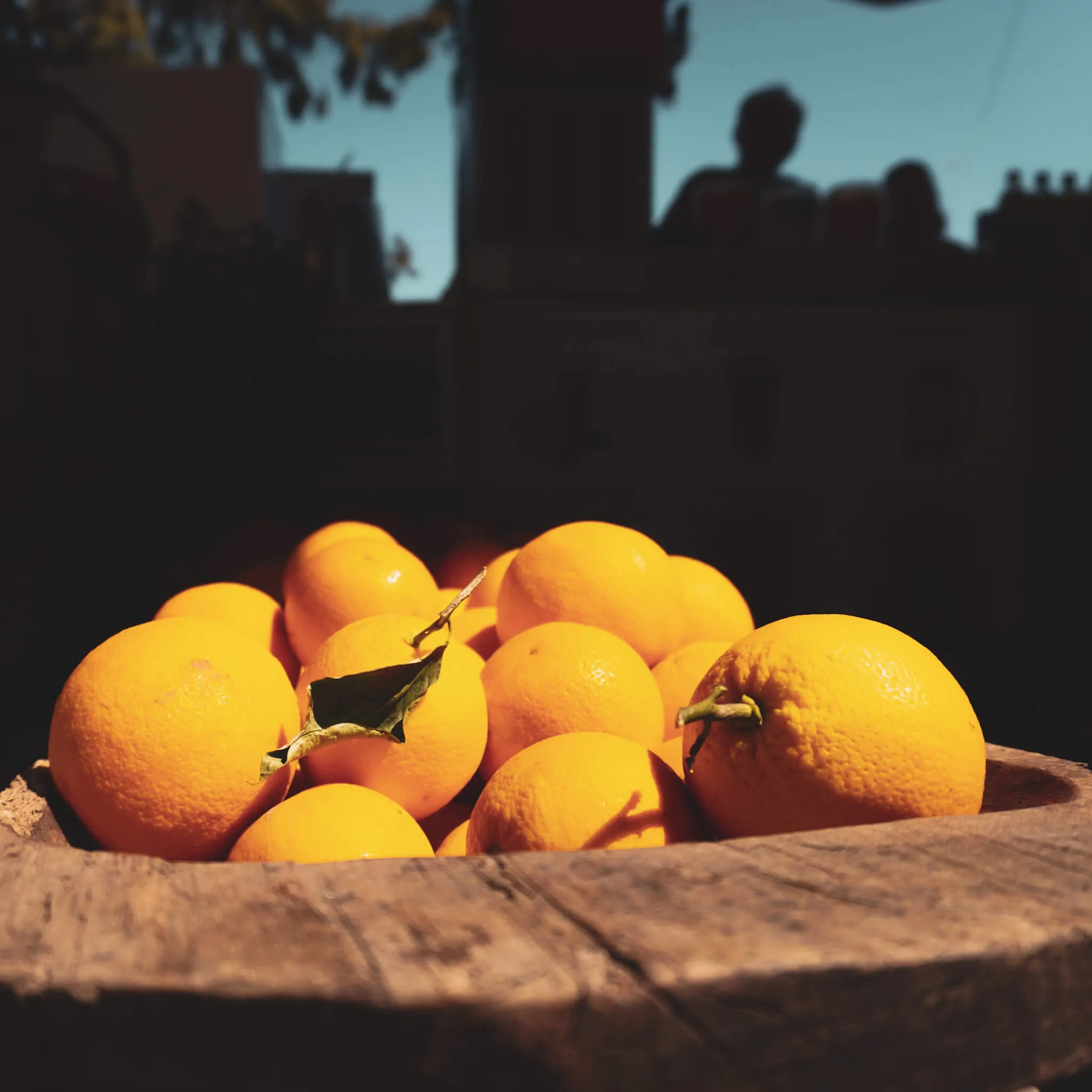 Frische Orangen liegen in einer rustikalen Holzschale, arrangiert auf einer dunklen Oberfläche.