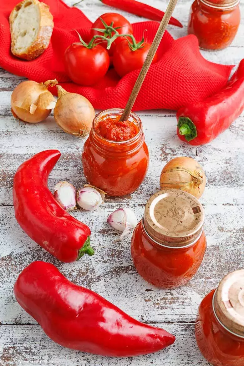 Frische Zutaten für Ajvar: Rote Spitzpaprika, reife Tomaten und Zwiebeln auf einem Holzbrett