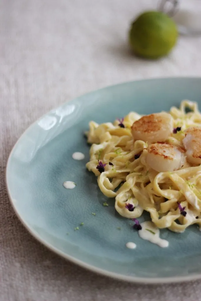 Frische Zutaten für das Jakobsmuscheln Rezept: Limette, Petersilie, Knoblauch und Jakobsmuscheln vor der Zubereitung.