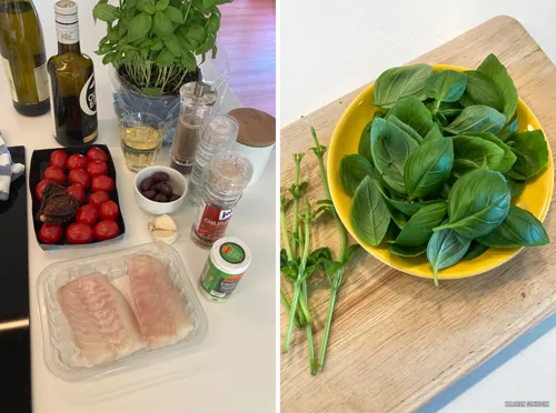 Frische Zutaten für das mediterrane Fischgericht: eine Handvoll Basilikum, Kirschtomaten, Oliven und Knoblauch auf einem Holzbrett bereit zur Zubereitung.