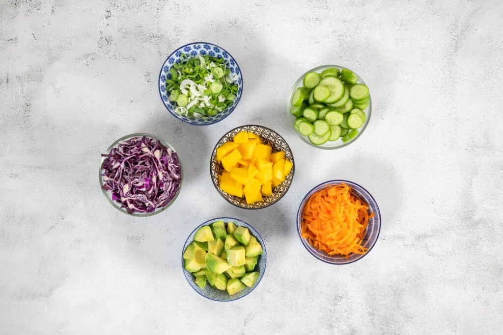 Frische Zutaten für eine Poke Bowl: Geschnittene Mango, Rotkohl, Avocado und Karotte