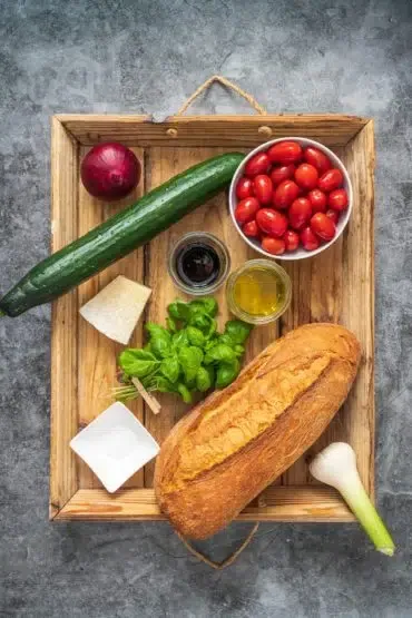 Frische Zutaten für Panzanella: reife Tomaten, Gurke, Basilikum und Ciabatta bereit zum italienischen Brotsalat zubereiten