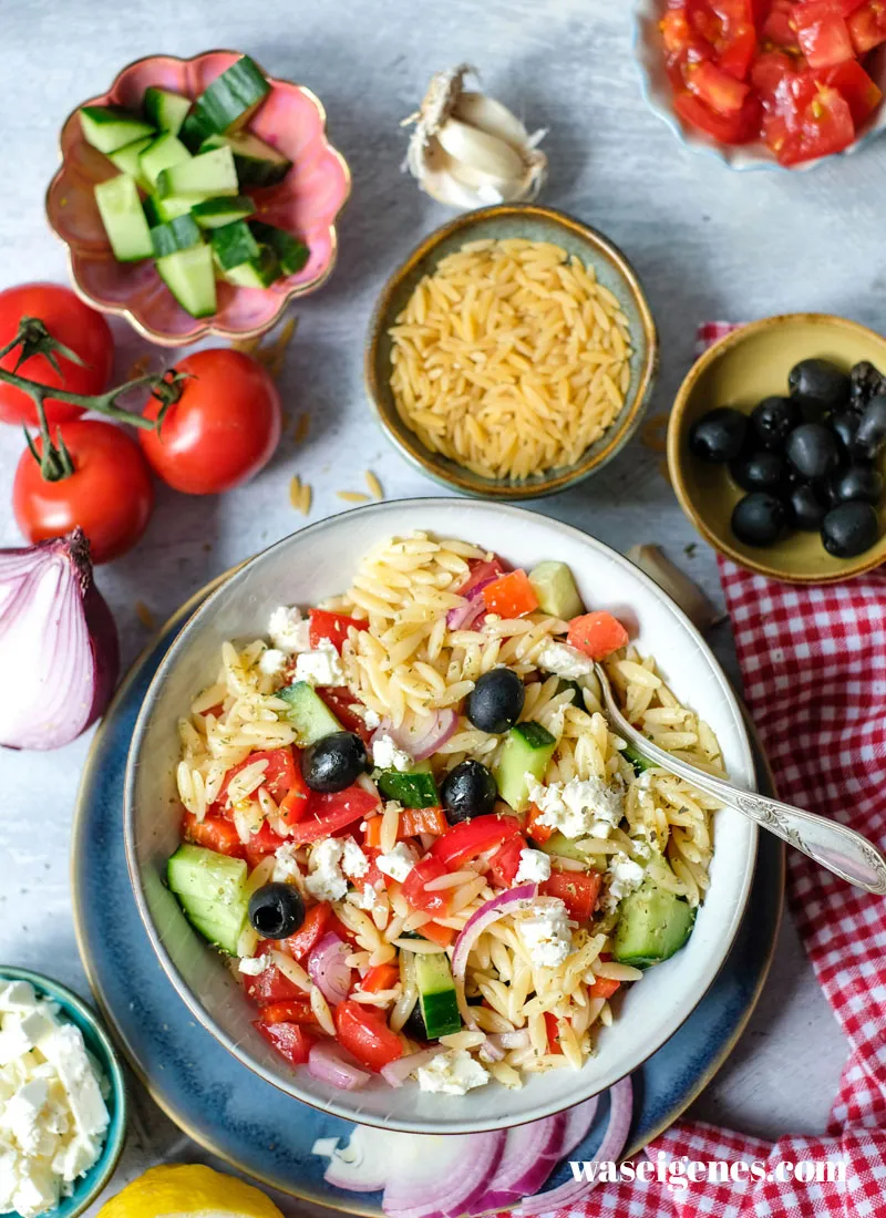 Frischer griechischer Nudelsalat mit Kritharaki, Feta, Gurke und Oliven, angerichtet in einer Holzschale.