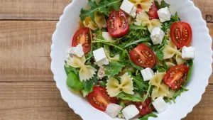 Frischer Nudelsalat mit Feta, Rucola, Cherrytomaten und Dressing in einer großen Schüssel