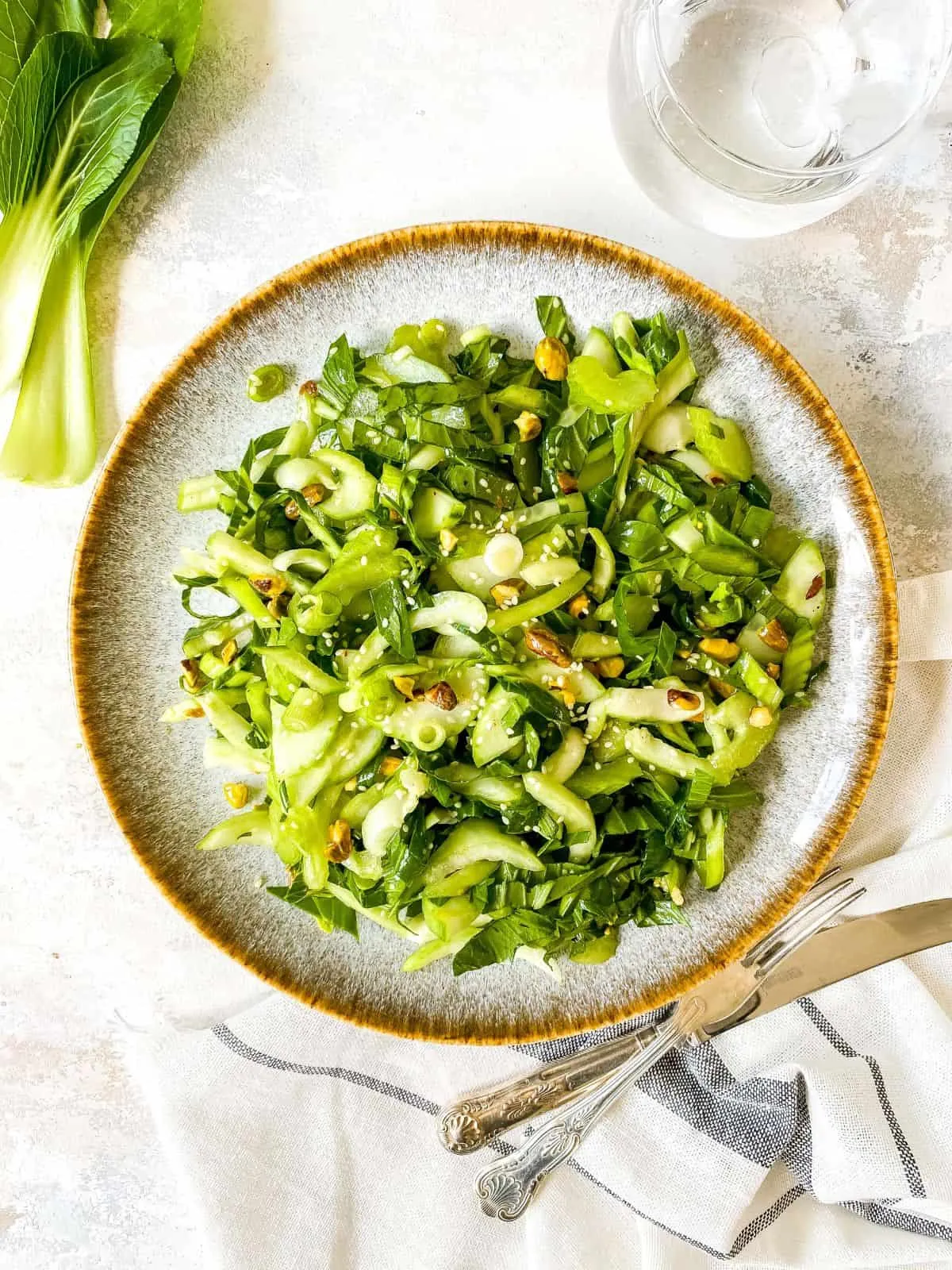 Frischer Pak Choi Salat angerichtet auf einem modernen grauen Teller mit blau gestreiftem Geschirrtuch.