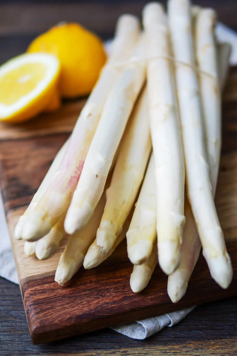 Frischer weißer Spargel neben einer halbierten Zitrone auf einem rustikalen Holzbrett, bereit zur Zubereitung für einfache Spargelrezepte.