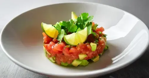 Frisches Avocado-Tomaten-Tatar mit Limettensaft, serviert in einer Schale, garniert mit Limettenscheiben und frischen Kräutern.