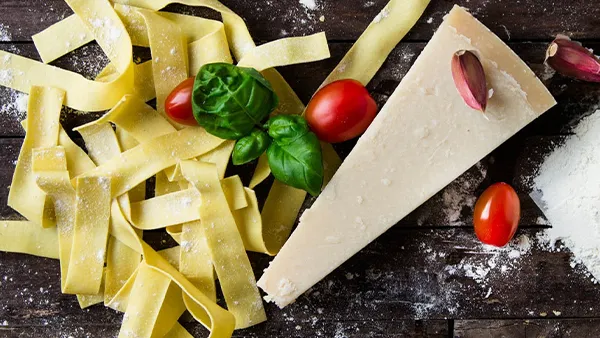 Frisches Basilikum, Knoblauch, Olivenöl, Pasta, Parmesan, Tomaten und Zitrone auf einem Holztisch, als Symbole der italienischen Küche.