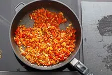 Frisches Gemüse wie Paprika, Tomaten, Zwiebeln und Knoblauch werden in einer Pfanne angedünstet, um ihr volles Aroma zu entfalten.