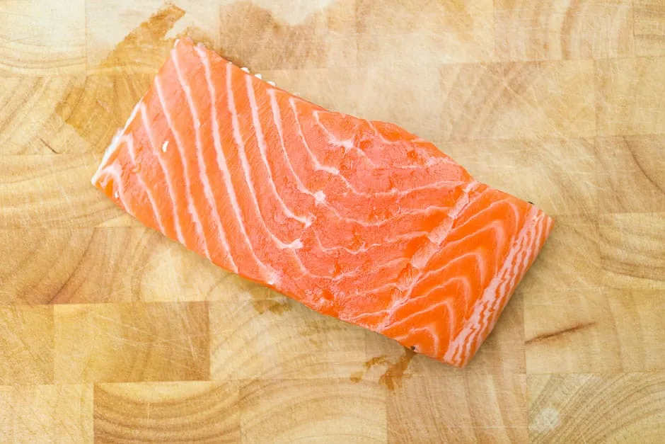 Frisches Lachsfilet auf einem Holzbrett, bereit für die Zubereitung gesunder Gerichte zum Abnehmen