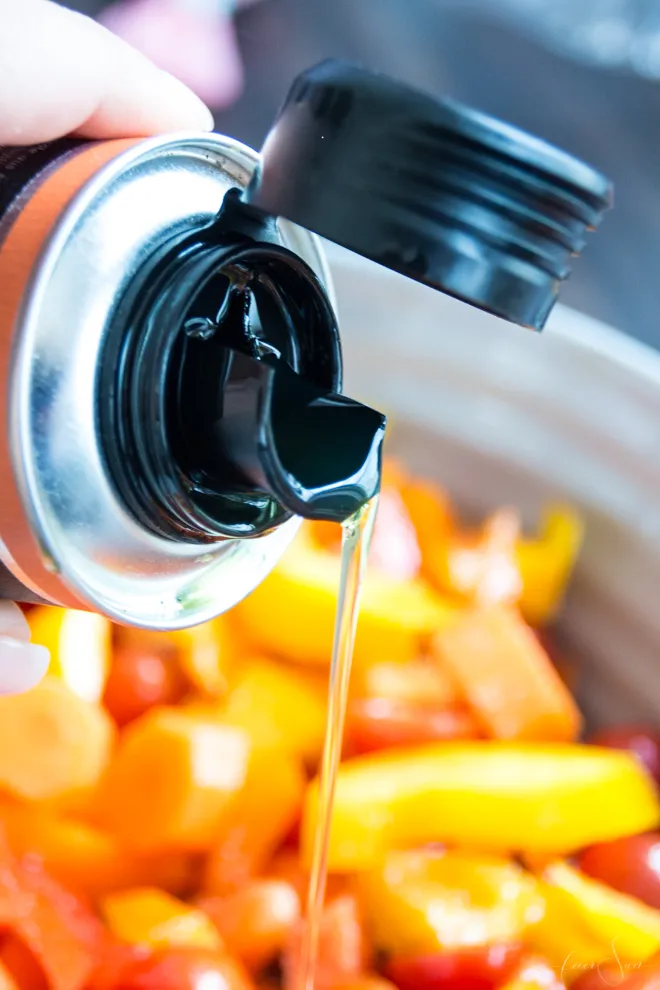 Frisches Olivenöl wird über geschnittenes Gemüse gegossen, als Vorbereitung für ein gesundes Ofengemüse mittagessen.