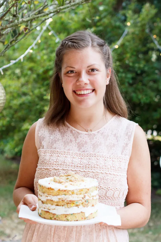 Fröhliche Frau hält ein Stück Funfetti Kuchen, strahlt und feiert ihren Geburtstag