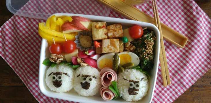 Fröhliche japanische Bento-Box mit Reisbällchen und Gemüse