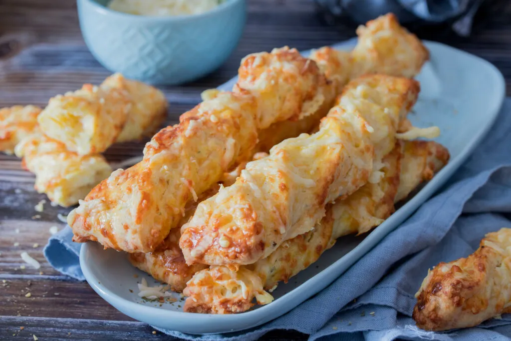 Gebackene Käsestangen liegen golden auf Backpapier, bereit als gesundes und beliebtes herzhaftes Gebäck für die ganze Familie.
