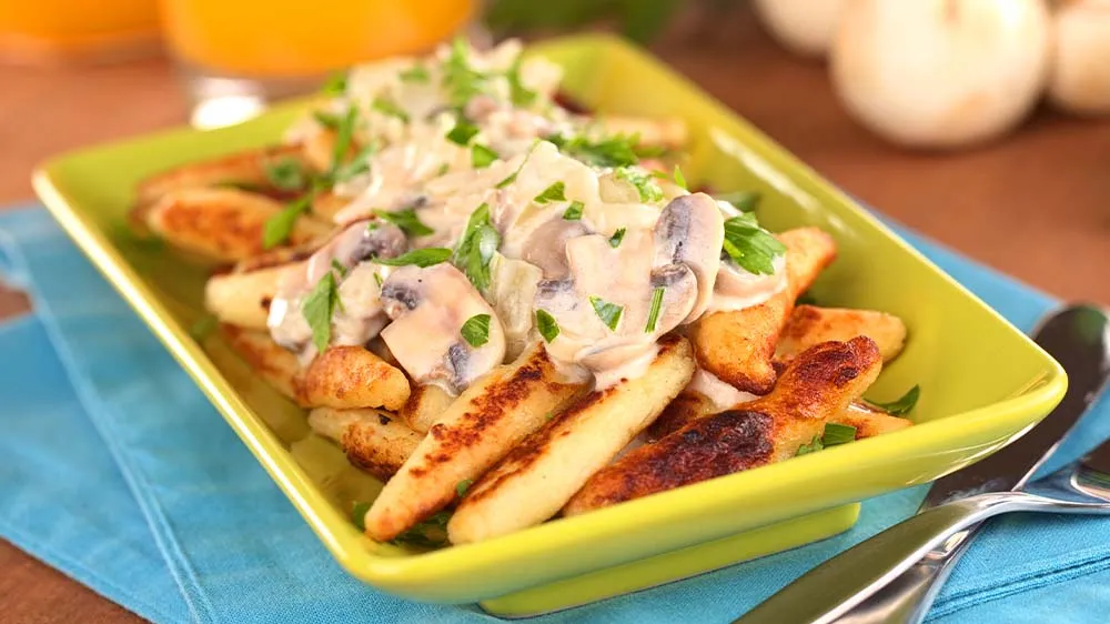 Gebratene Schupfnudeln mit Pilzen und frischen Kräutern in einer Pfanne.