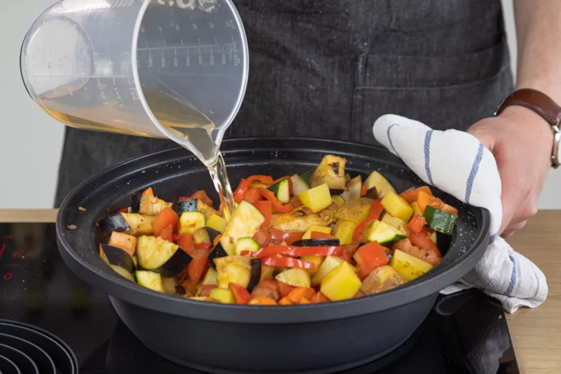 Gemüsebrühe wird über das angebratene Gemüse in der Tajine gegossen