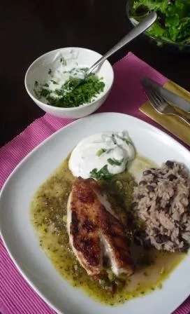 Gericht Jamie Oliver Jamaica-Hähnchen mit Reis und Bohnen auf einem Teller, mit Joghurt-Dip und Salat im Hintergrund.