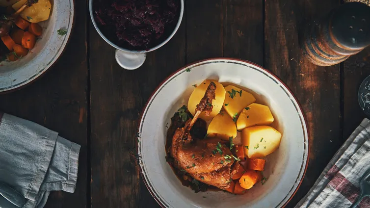 Geschmortes Kaninchen auf einem Teller, umgeben von klassischen Beilagen wie Salzkartoffeln, Rotkohl und glasierten Möhren, perfekt für ein festliches Mahl