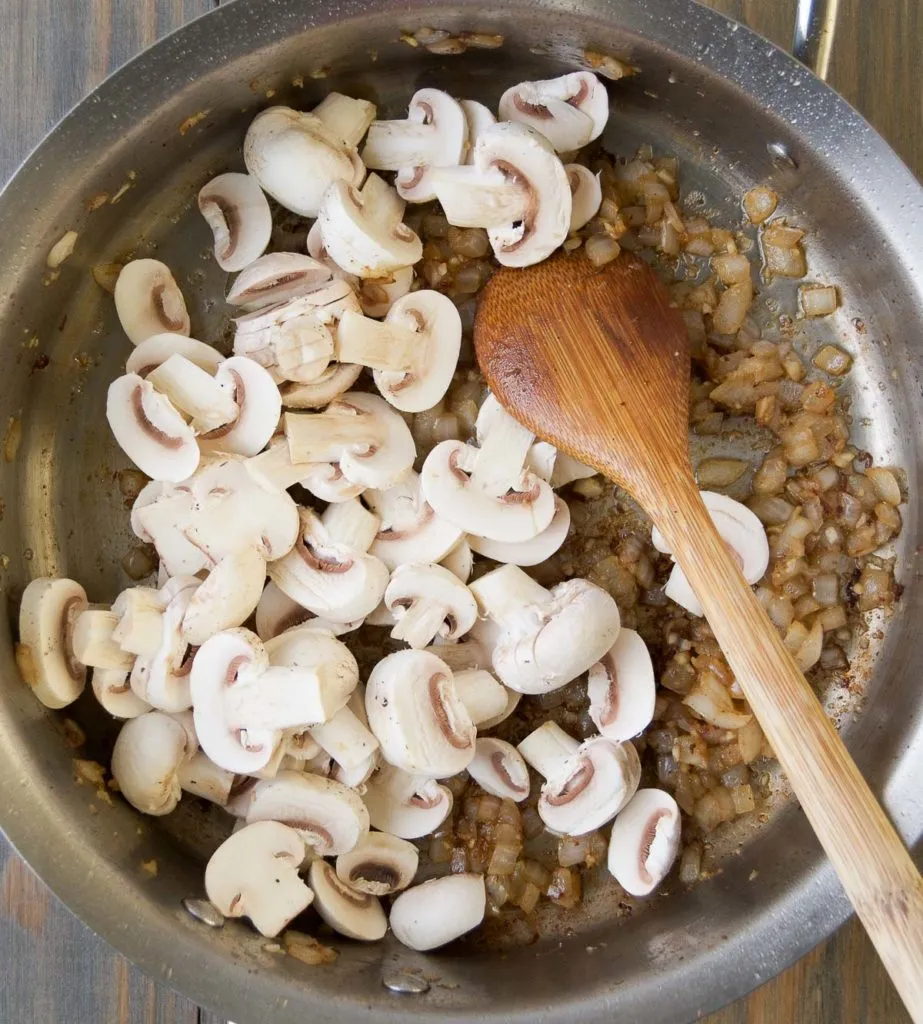 Geschnittene Champignons zu den Zwiebeln in die Pfanne geben